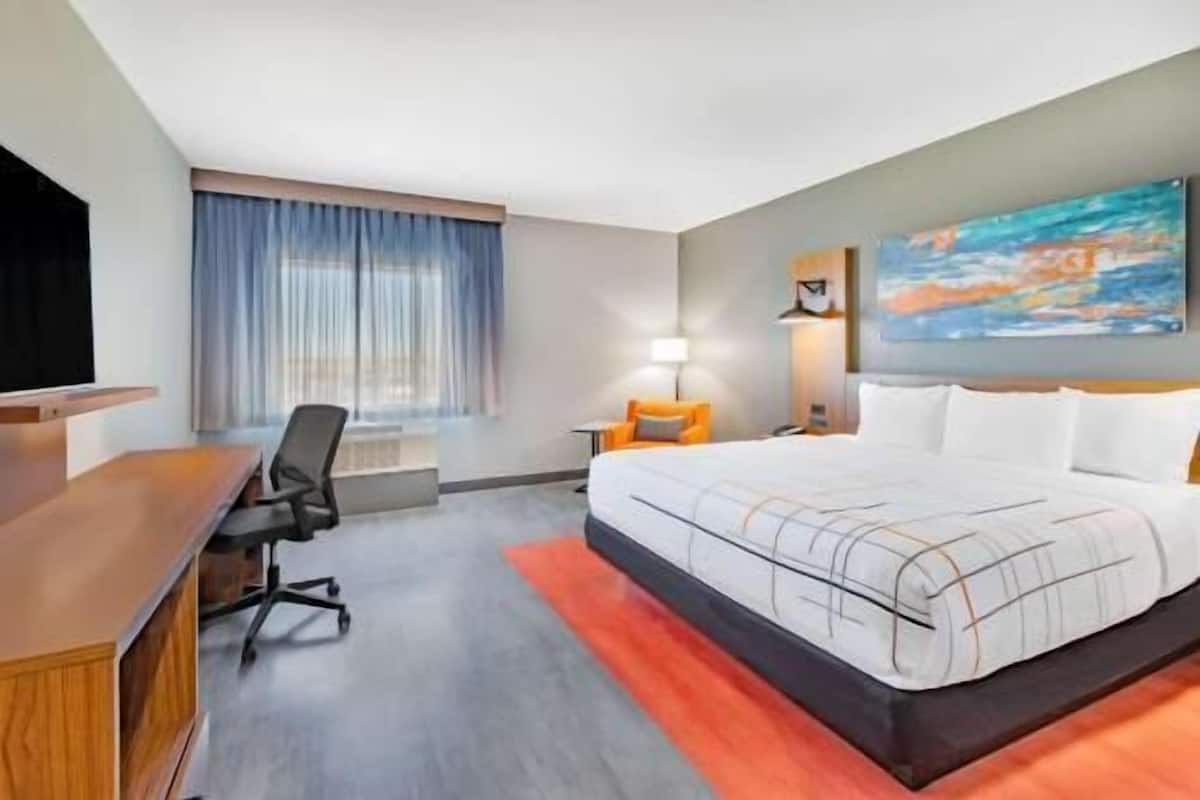Een hotelkamer met een bed, bureau, stoel, lamp en een schilderij aan de muur.