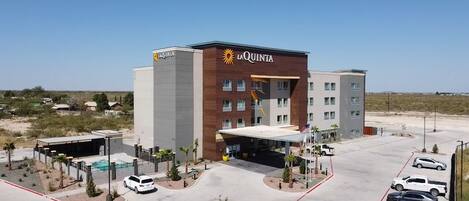 Un hôtel avec une enseigne « La Quinta » bien visible, un parking avec plusieurs voitures et un petit espace piscine.