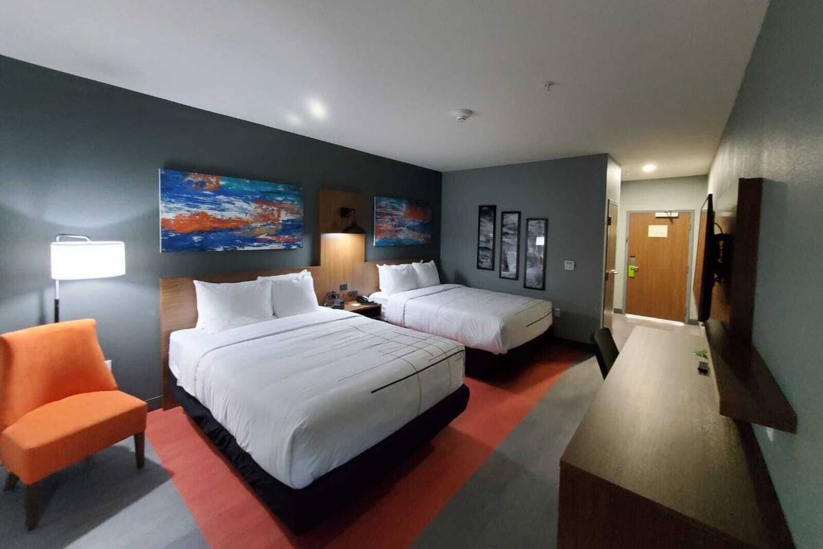 Een hotelkamer met twee bedden, een bureau, een stoel en kunstwerken aan de muur.