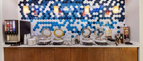 A hotel bathroom with a modern design, featuring a blue and white hexagonal tile wall, multiple sinks, and a coffee machine.