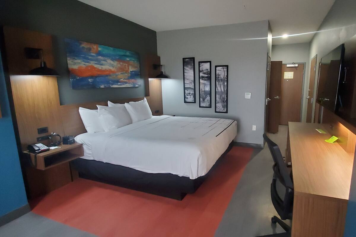 Een hotelkamer met een groot bed, nachtkastjes, een bureau, een stoel, een televisie en kunstwerken aan de muren.