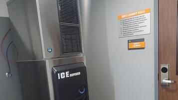 Habitación de hotel con un equipo de aire acondicionado metálico, dispensador de hielo y un cartel que detalla las normas de lavandería para huéspedes.