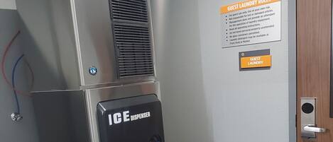 A hotel room with a metallic air conditioning unit, an ice dispenser, and a sign detailing guest laundry rules.