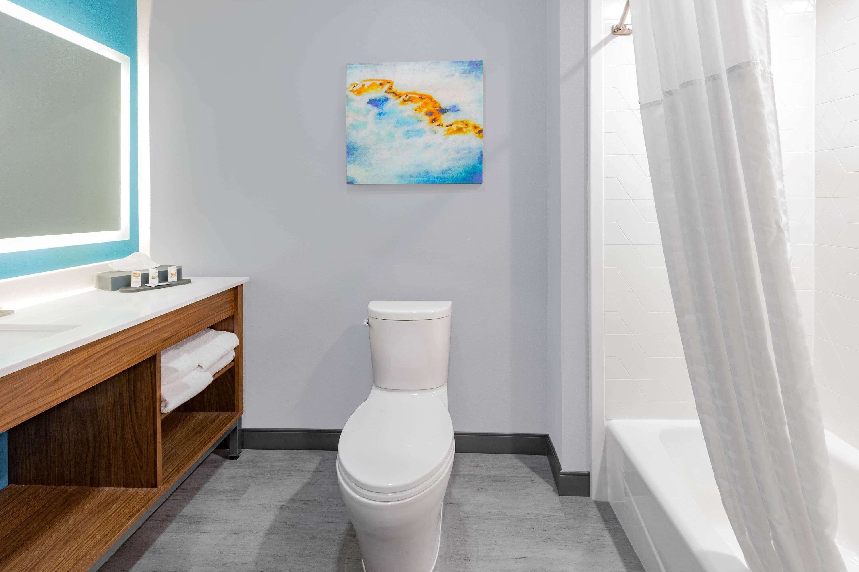 A modern bathroom with a white toilet, a wooden vanity, a large mirror, and a shower curtain.