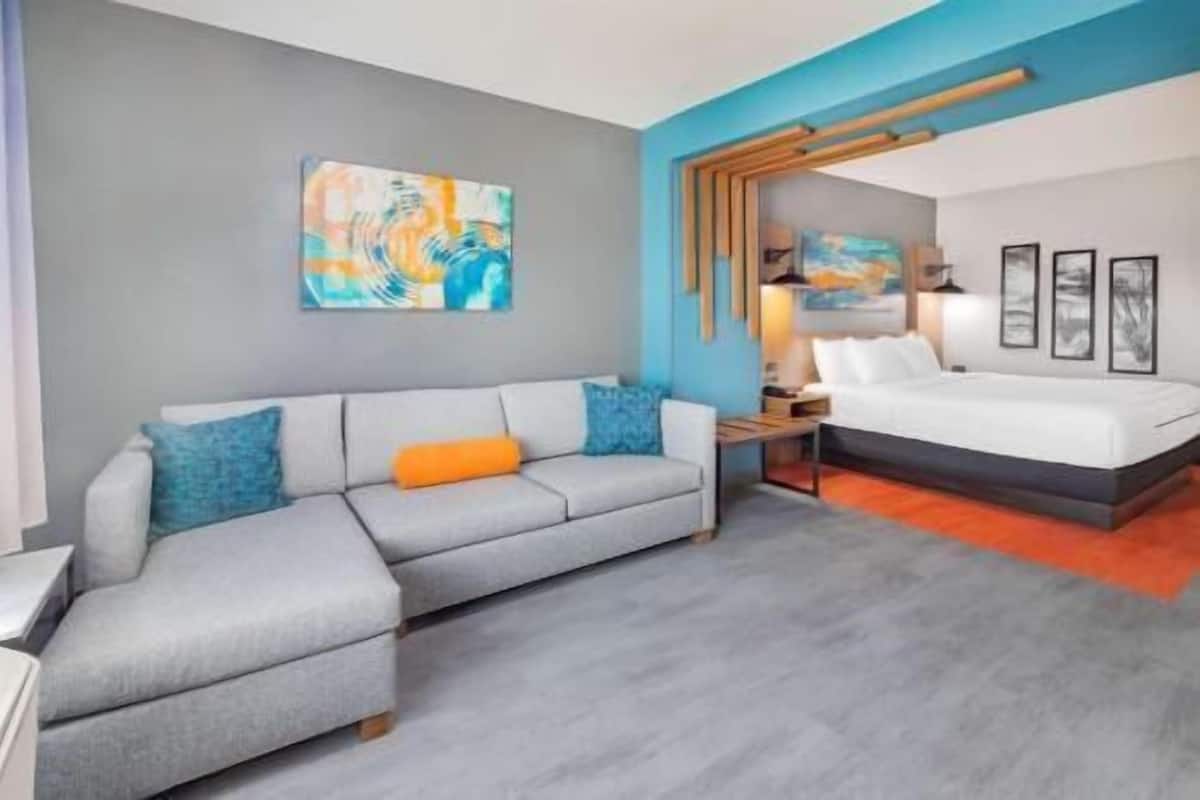 Een moderne hotelkamer met een grijze bank, een bed en abstracte kunst aan de muren.