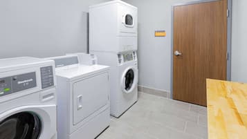 A laundry room with two front-loading machines, a wooden door, and a sign indicating the room is for electric appliances.