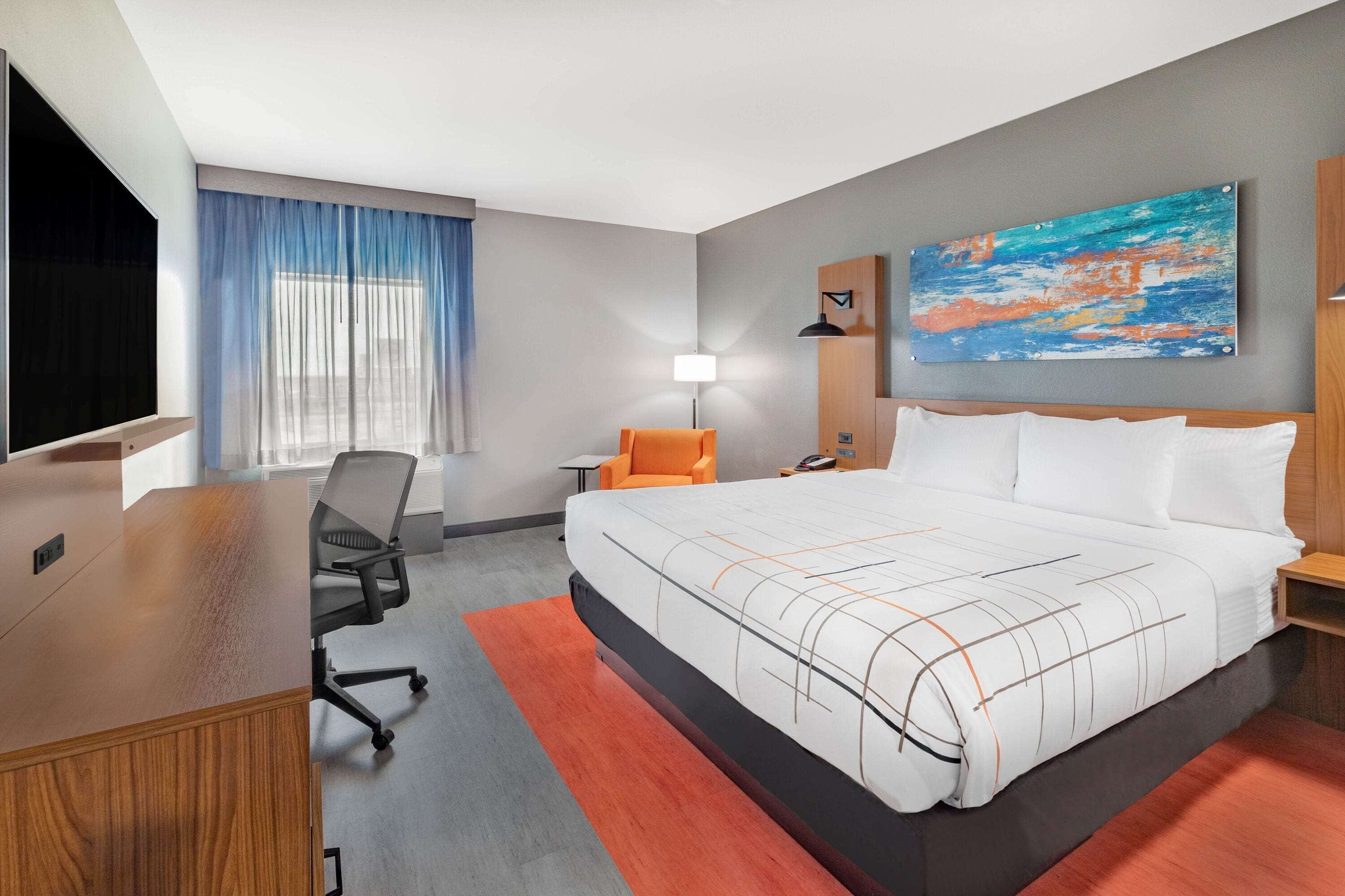 A hotel room with a large bed, a desk, a chair, a lamp, and a painting on the wall.