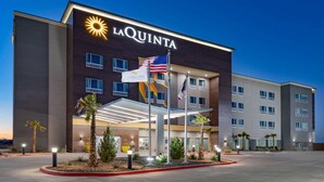 Un hôtel La Quinta au design moderne, avec un logo solaire bien visible, plusieurs drapeaux et une entrée bien éclairée.