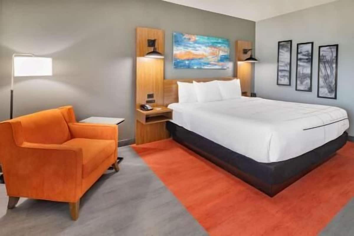 Een hotelkamer met een bed, bureau, stoel, lamp en kunst aan de muur.