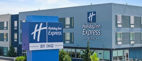 A Holiday Inn Express hotel with a modern design, featuring a prominent blue and white color scheme, large windows, and a clear sky.