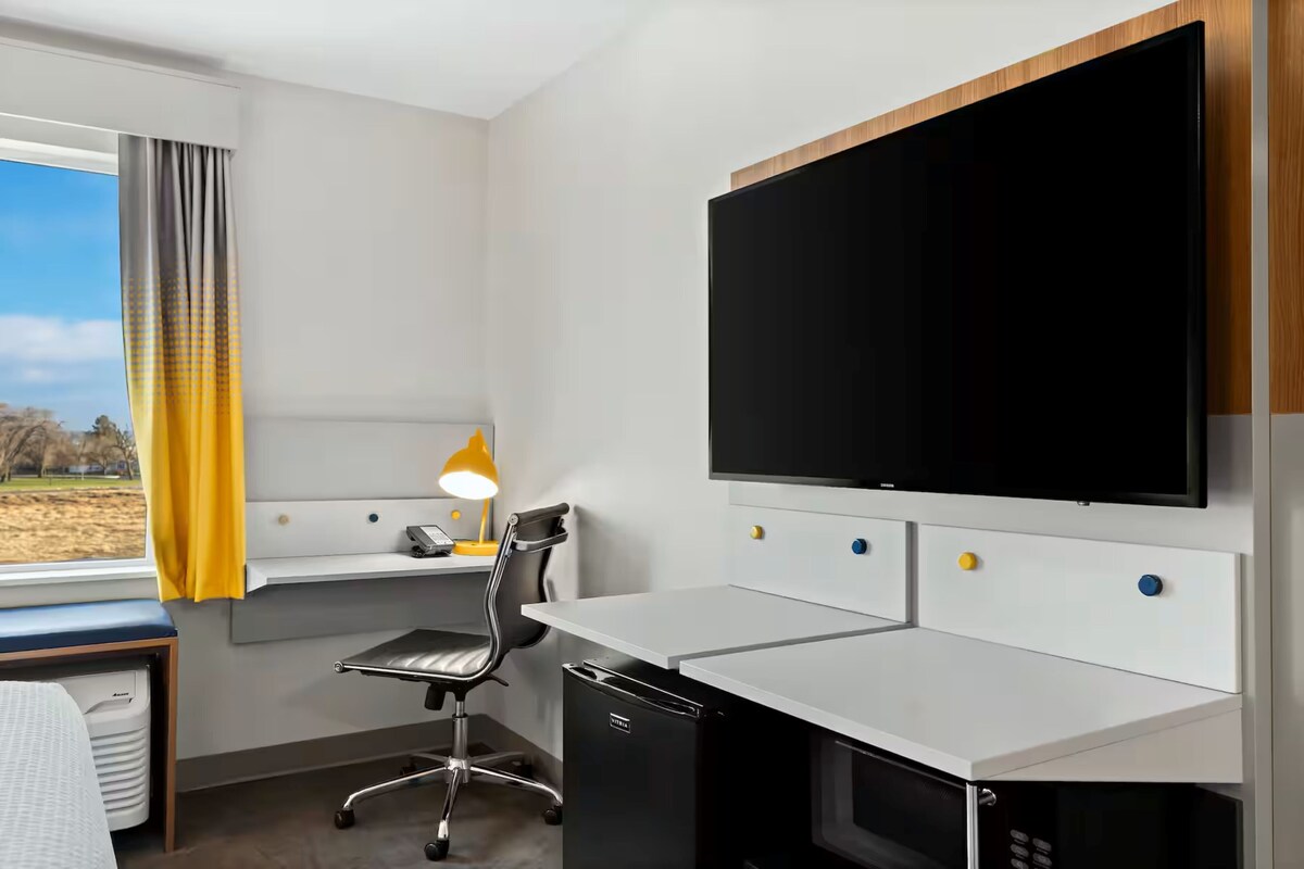 A modern hotel room with a desk, chair, and a large flat-screen TV mounted on the wall.