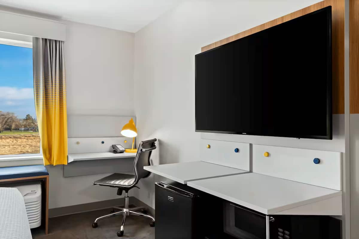 A modern hotel room with a desk, chair, and a large flat-screen TV mounted on the wall.