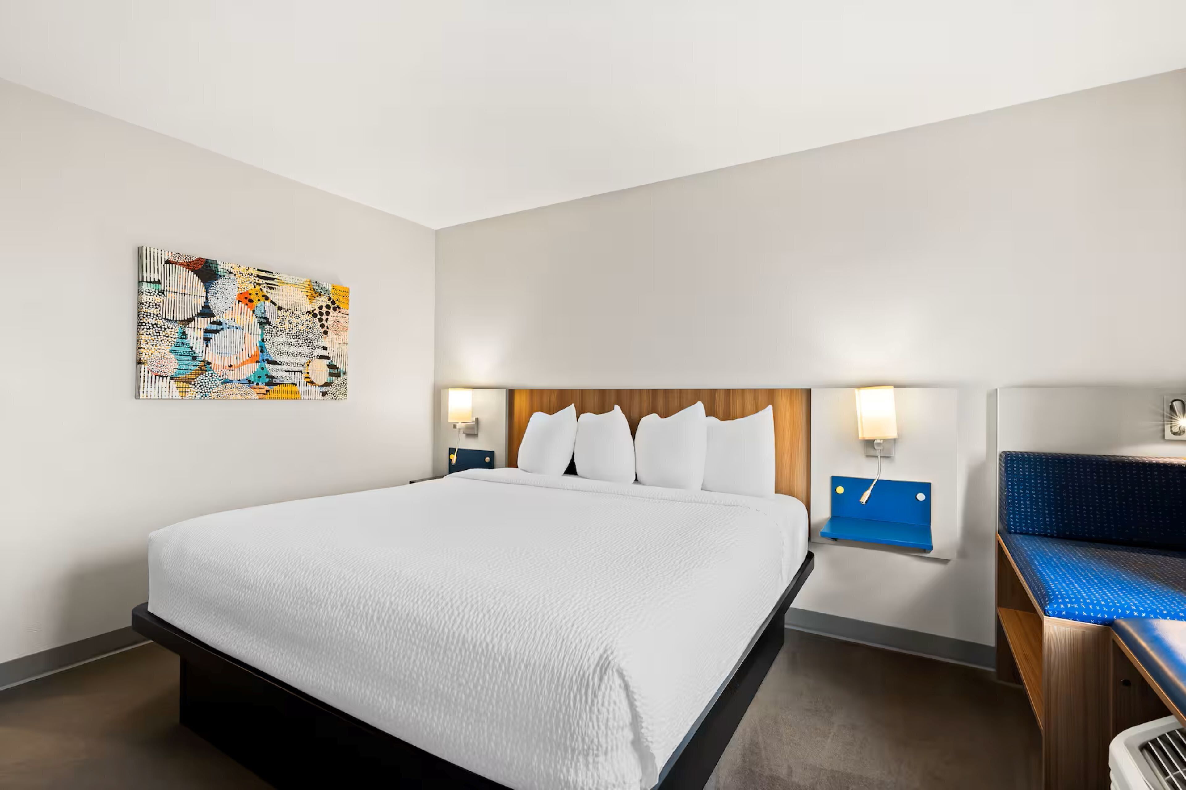 Une chambre d’hôtel avec un grand lit, un banc bleu et une œuvre d’art accrochée au mur.