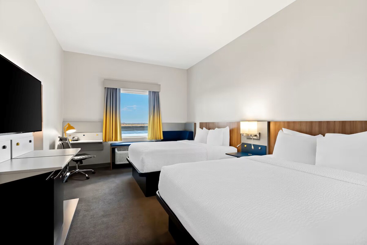 A hotel room with two beds, a desk with a chair, a TV, and a window with curtains.