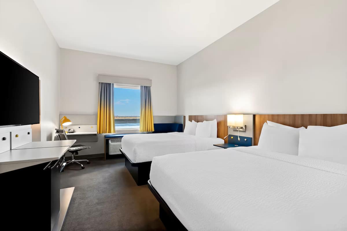 A hotel room with two beds, a desk with a chair, a TV, and a window with curtains.