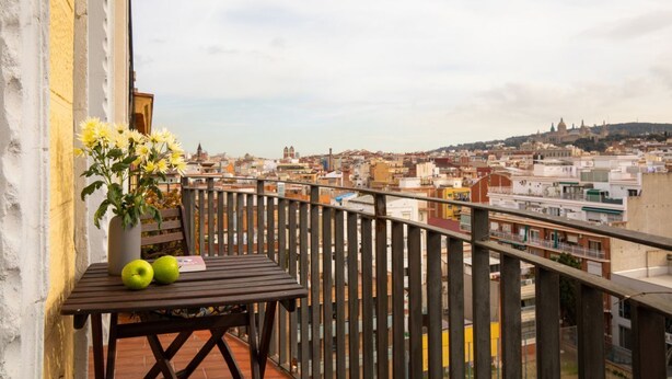 A balcony with a view of a cityscape, a table with apples and a vase of flowers, and a wooden chair. - Casa Cosi - Sants Barcelona (Barcelona)