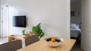 A modern living room with a flat-screen TV mounted on the wall, a dining table with a bowl of fruit, and a large green plant. - Casa Cosi - Sants Barcelona (Barcelona)