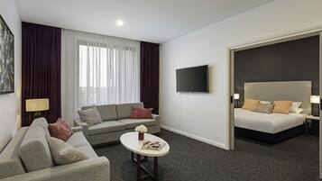 A hotel room with a sofa, a coffee table, a TV, a bed, and a view through a door.
