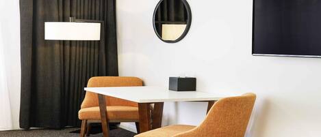 A room with a white table, two orange chairs, a black-framed mirror, a black TV, and a black curtain.