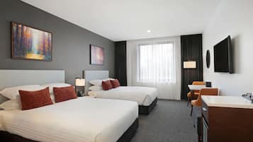 Een hotelkamer met twee bedden, een bureau, een stoel, een televisie en kunstwerken aan de wand.