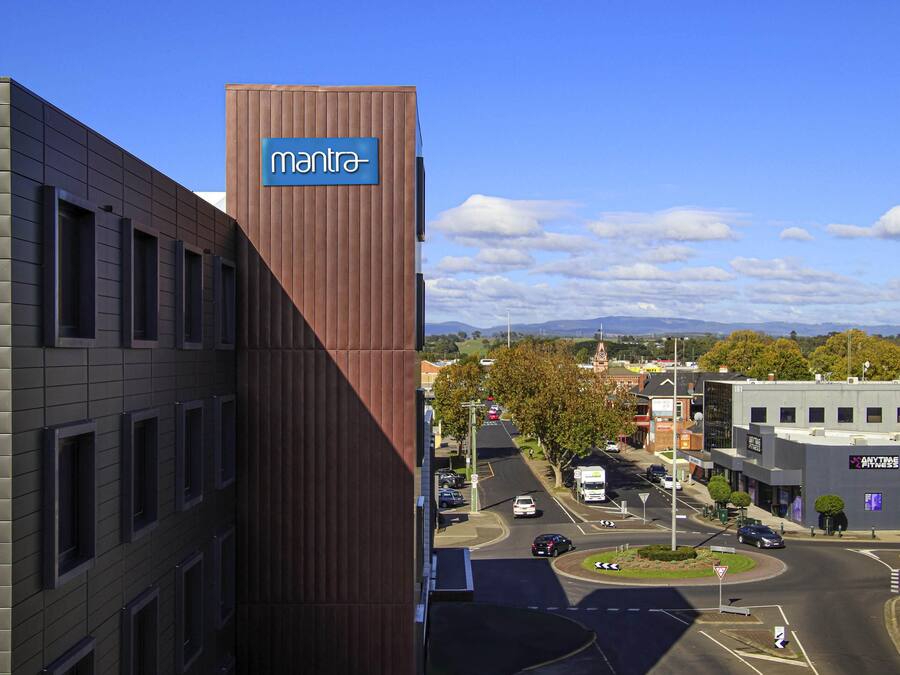 Un edificio con un letrero que dice 'mantra', un estacionamiento y una vista de la calle con vehículos.