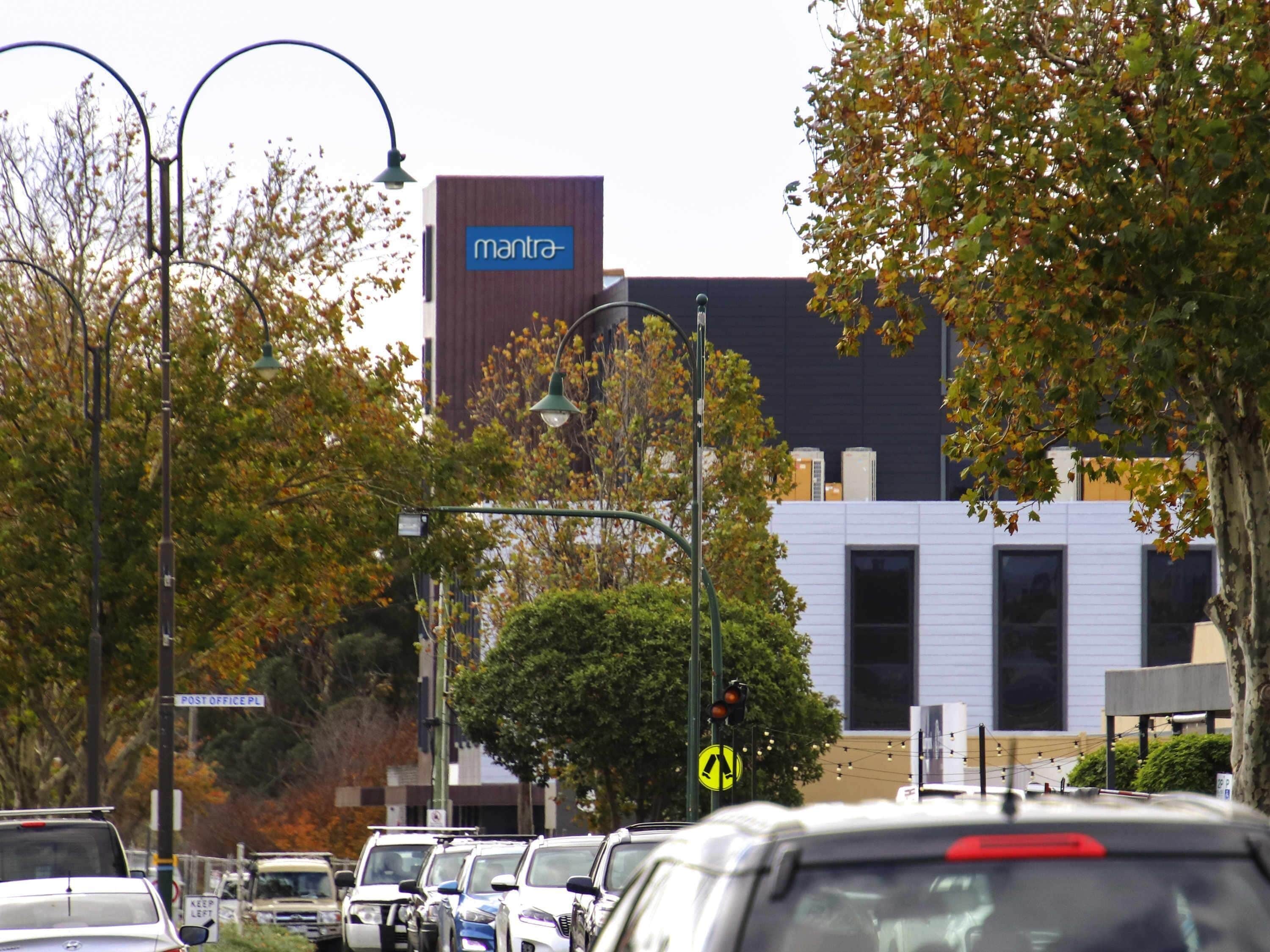 A street with parked cars, a building with a sign reading 'mantra,' and a street sign for 'POST OFFICE PL.'