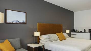 Habitació d'hotel moderna amb un llit gran, un sofà, una tauleta de nit, una làmpada i un quadre al mur.