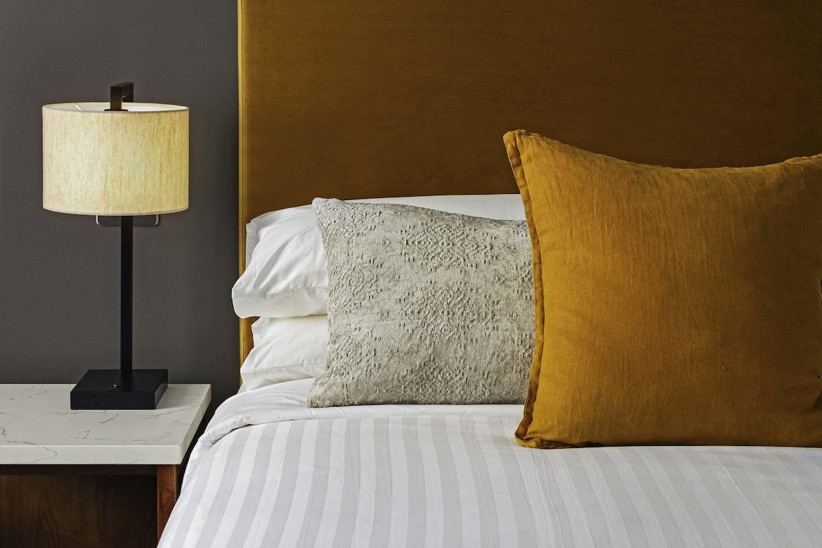 Una cama bien hecha con ropa de cama a rayas, una lámpara en una mesita de noche y un cabecero.