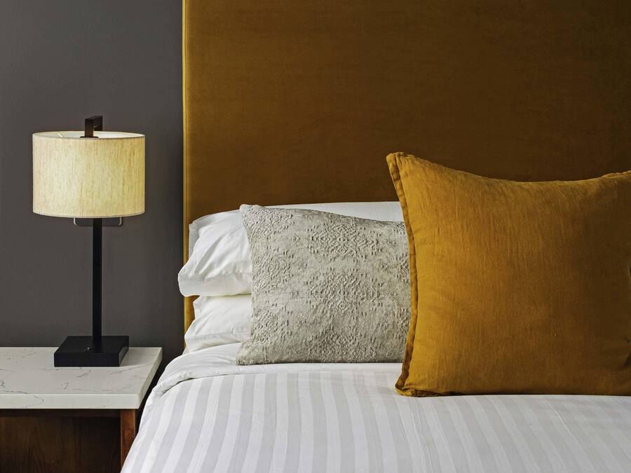 A neatly made bed with striped bedding, a lamp on a bedside table, and a headboard.