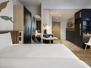 A modern hotel room with a large bed, a desk with a chair, a kitchenette, and a wardrobe. - Aparthotel Adagio Access Brussels Delta (Brussels)