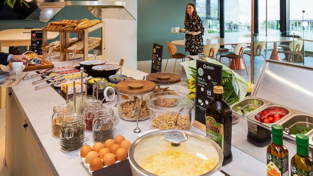 Zona de bufé con diversos alimentos y condimentos, incluyendo una olla grande de sopa, frascos de pepinillos y botellas de aceite de oliva.