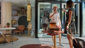 A modern hotel lobby with a central bar area, seating arrangements, and a large window providing a view of the outdoors. - Aparthotel Adagio Access Brussels Delta (Brussels)
