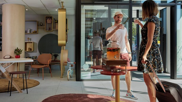 A modern hotel lobby with a central bar area, seating arrangements, and a large window providing a view of the outdoors. - Aparthotel Adagio Access Brussels Delta (Brussels)