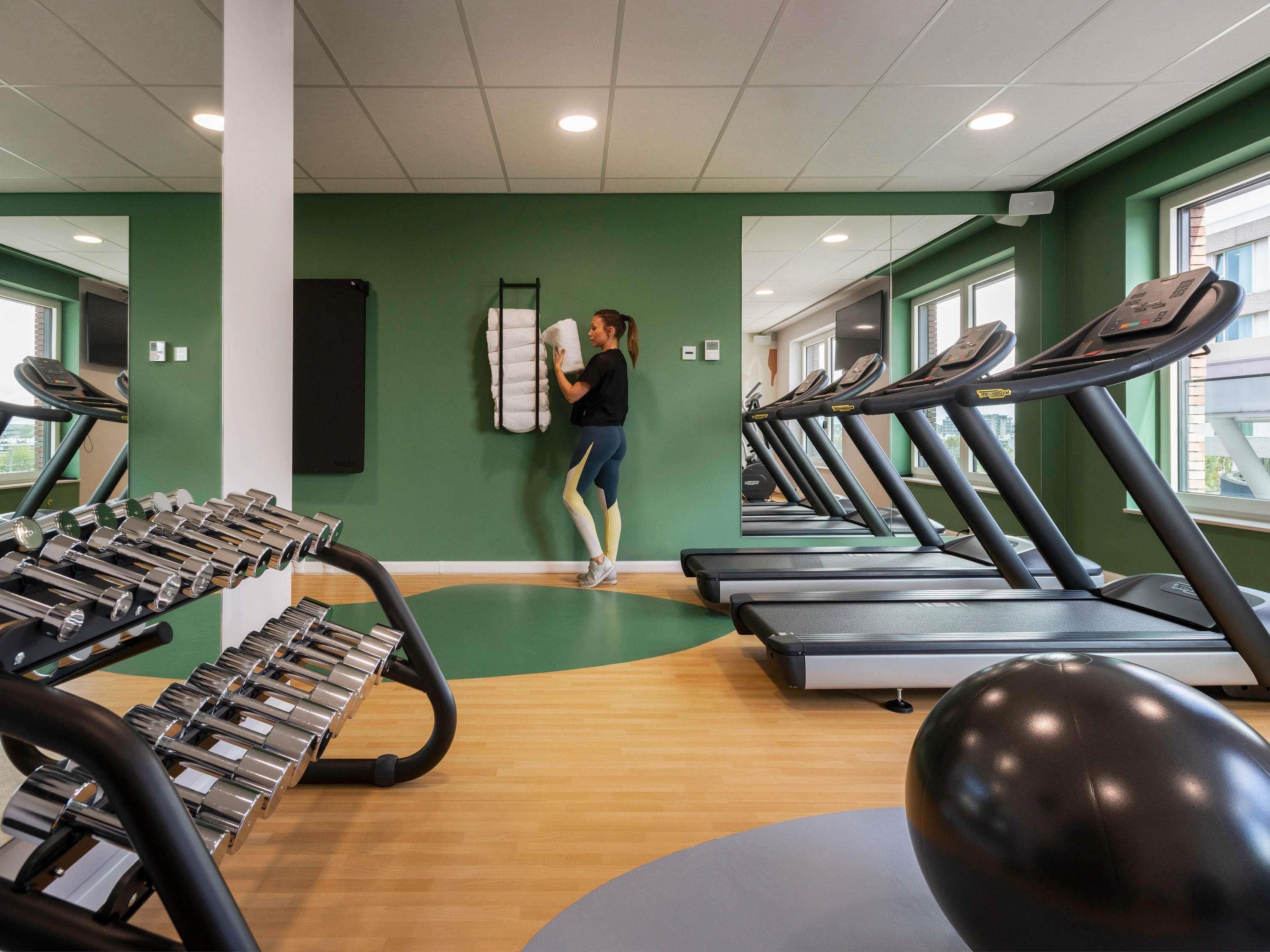 Ein Fitnessstudio mit Laufbändern, Hanteln und einer Person, die einen Handtuchhalter benutzt.