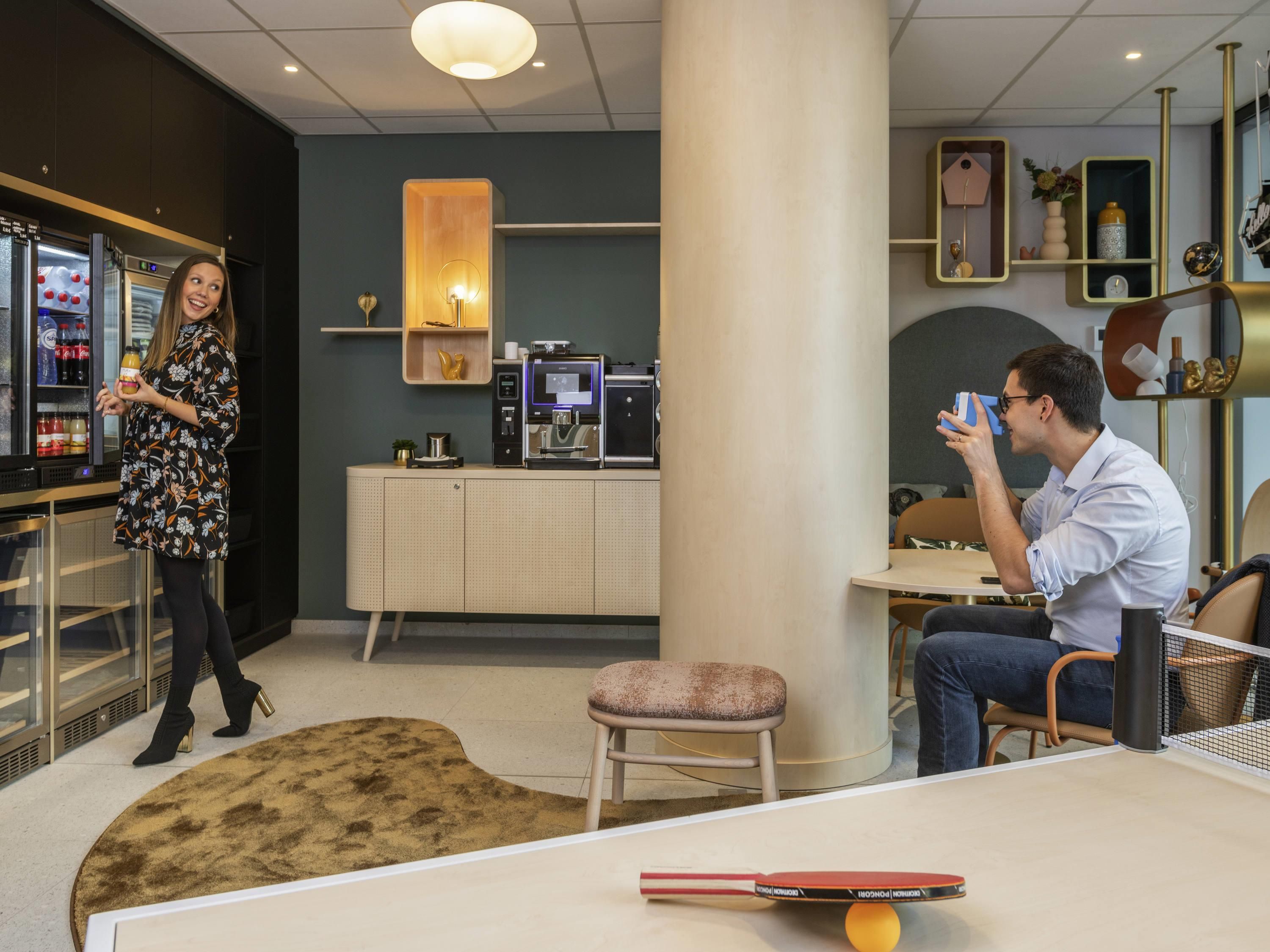 A modern hotel lobby with a bar area, a coffee machine, and a ping pong table.