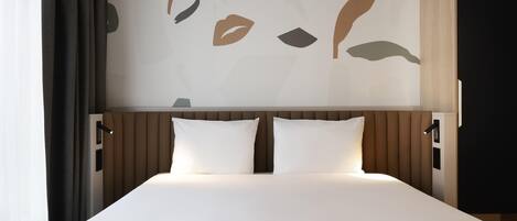 A hotel room with a bed, two pillows, a headboard, and a wall with abstract art.