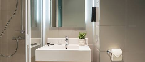 Un baño moderno con ducha de vidrio, un lavabo blanco con espejo encima y un inodoro a la derecha.