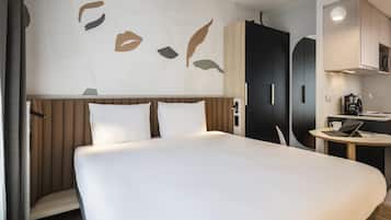 A hotel room with a large bed, a desk with a laptop, a wardrobe, and a kitchenette.