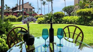 Une table en verre, avec deux verres à vin et une bouteille, entourée d’une végétation luxuriante et de palmiers.