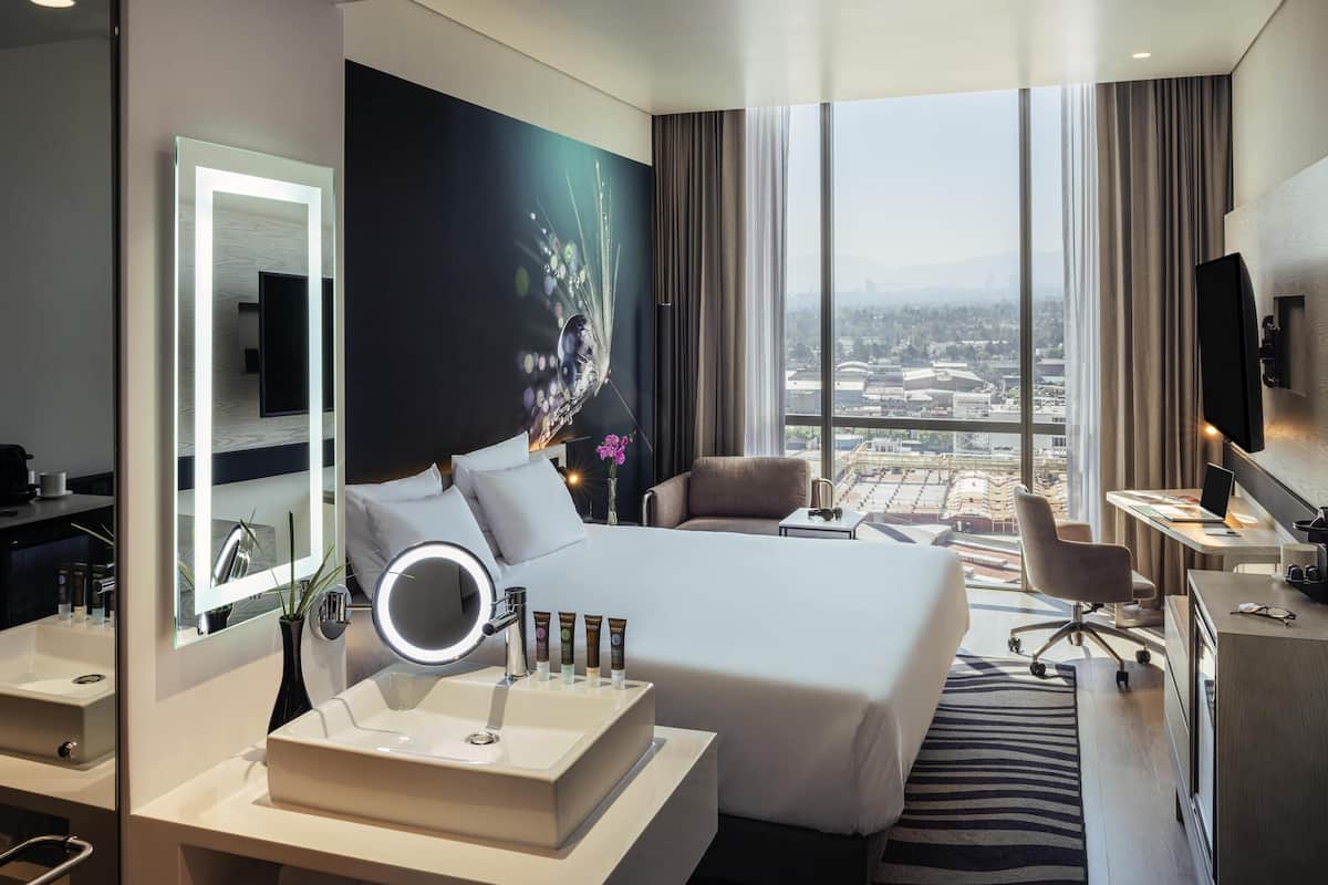 Una habitación de hotel moderna con una cama grande, un escritorio, un televisor y vistas a la ciudad.