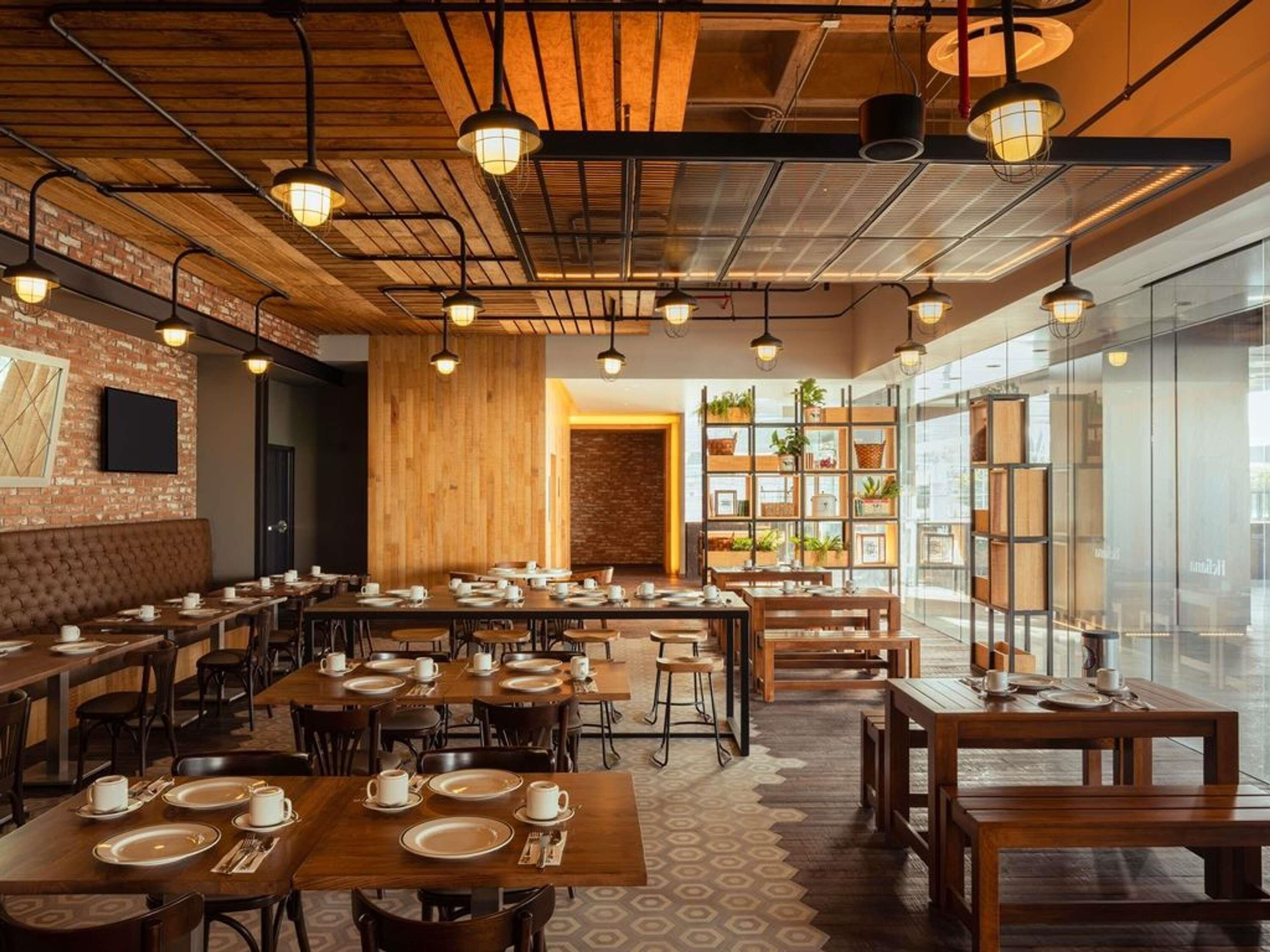 A restaurant with wooden tables and chairs, a brick wall, and hanging pendant lights.