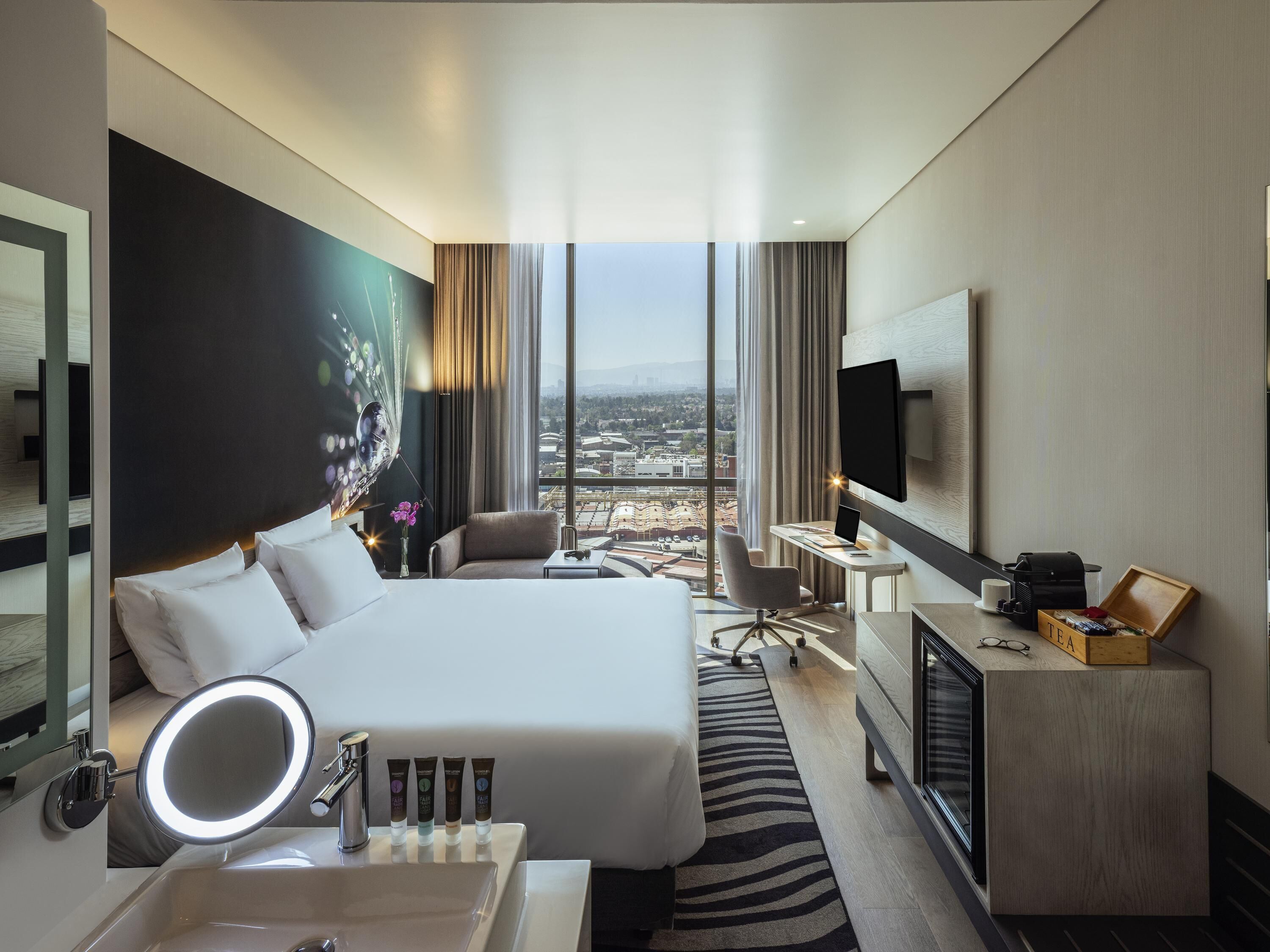 Habitación de hotel con una cama grande, un escritorio, un televisor y vistas a la ciudad.