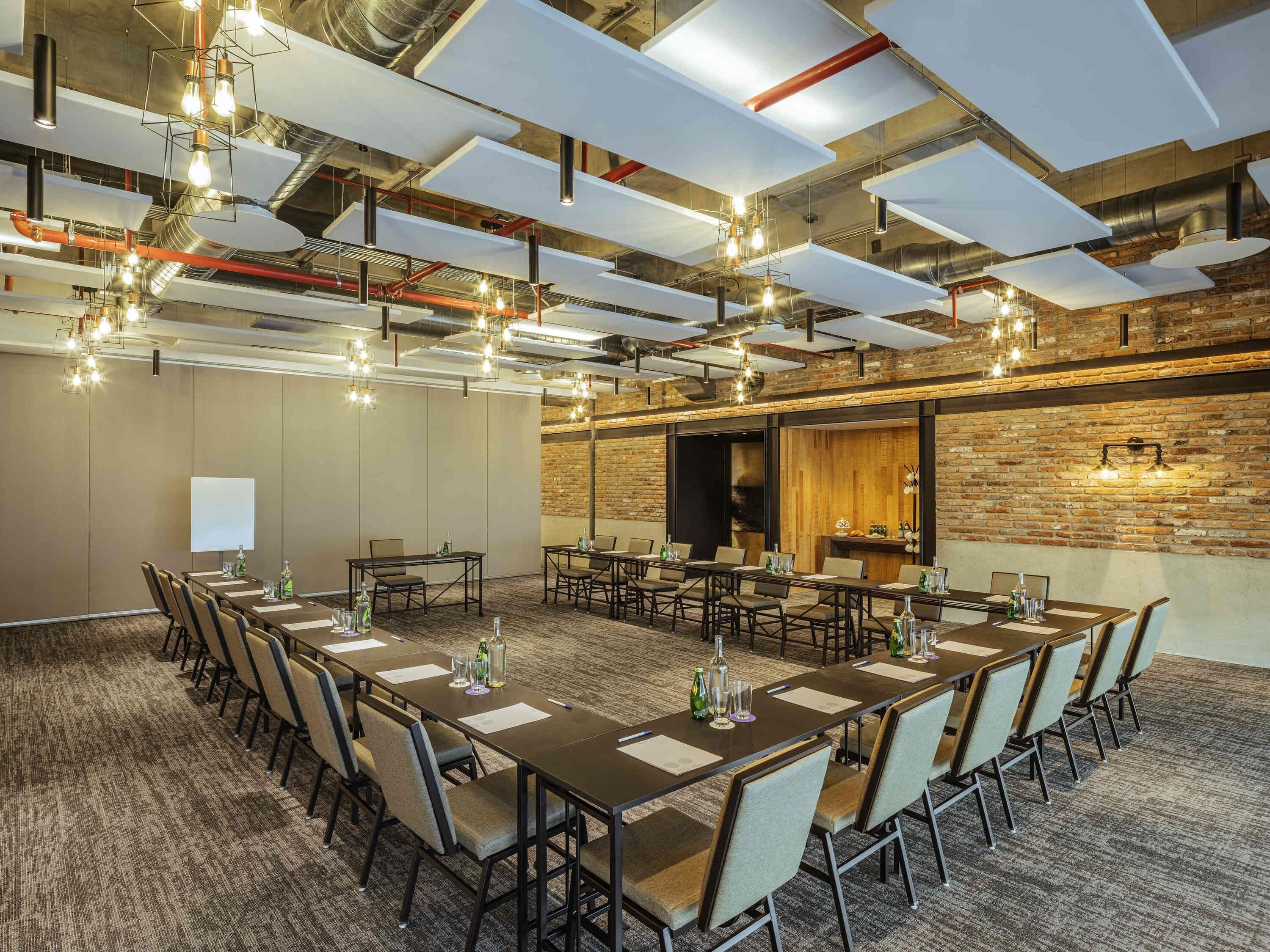 A conference room with long tables, chairs, and hanging light fixtures.