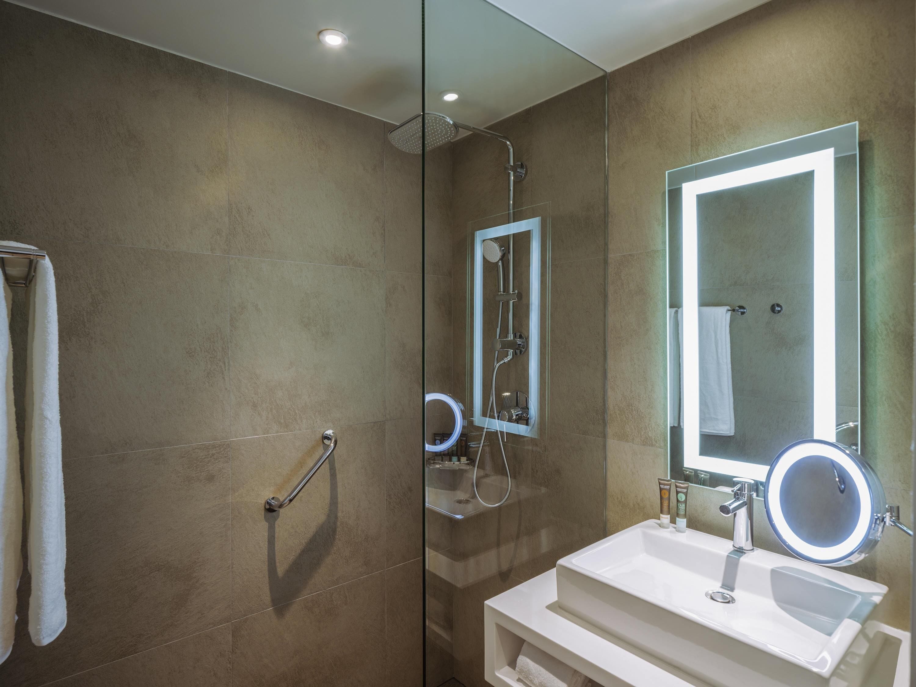 A modern bathroom with a glass shower enclosure, a white sink with a mirror, and a towel rack.
