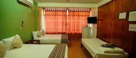 A hotel room with two single beds, a ceiling fan, an air conditioner, a television on a wooden cabinet, and a window with curtains.