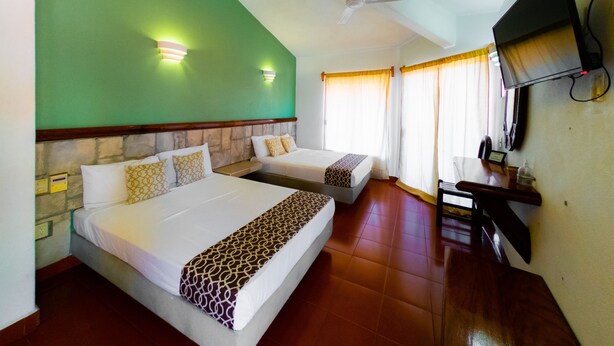 Habitación de hotel con dos camas, ventilador de techo, televisión y escritorio con teléfono.
