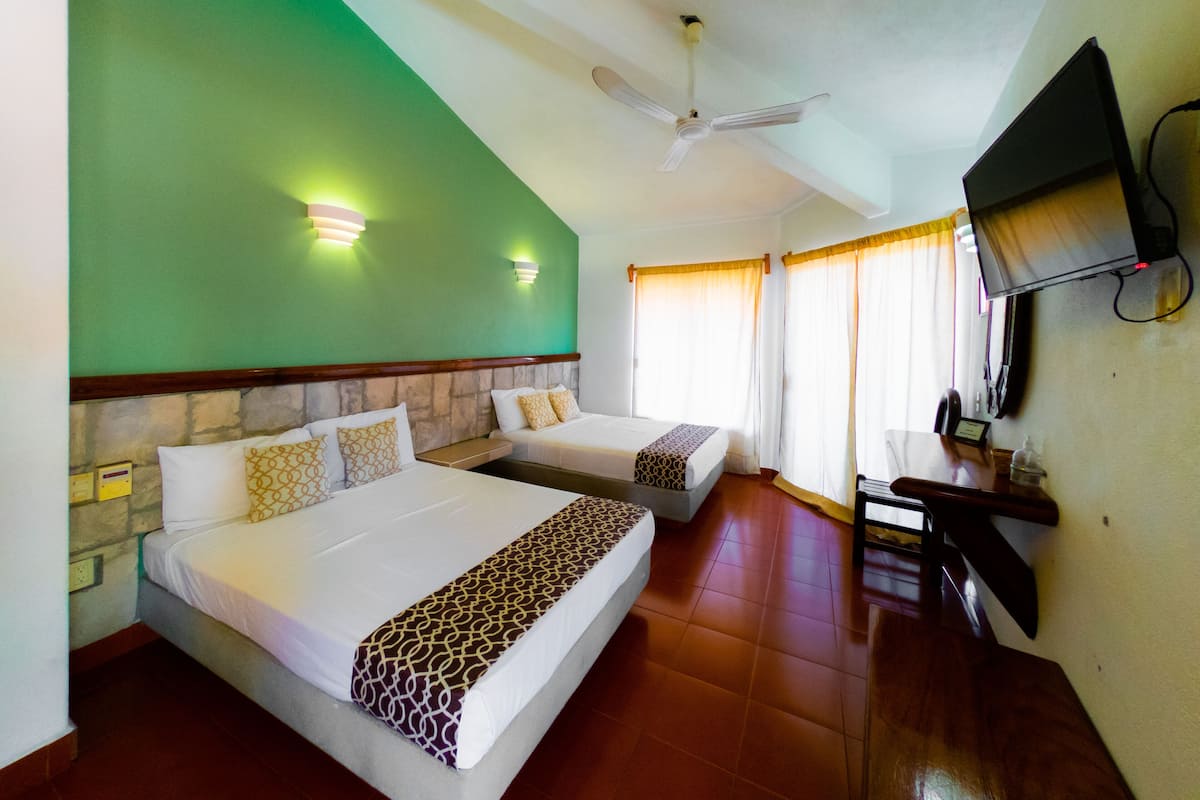 A hotel room with two beds, a ceiling fan, a TV, and a desk with a phone.