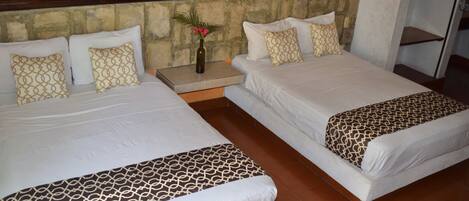 A hotel room with two beds, each with patterned bedding, a nightstand with a vase, and a stone accent wall.