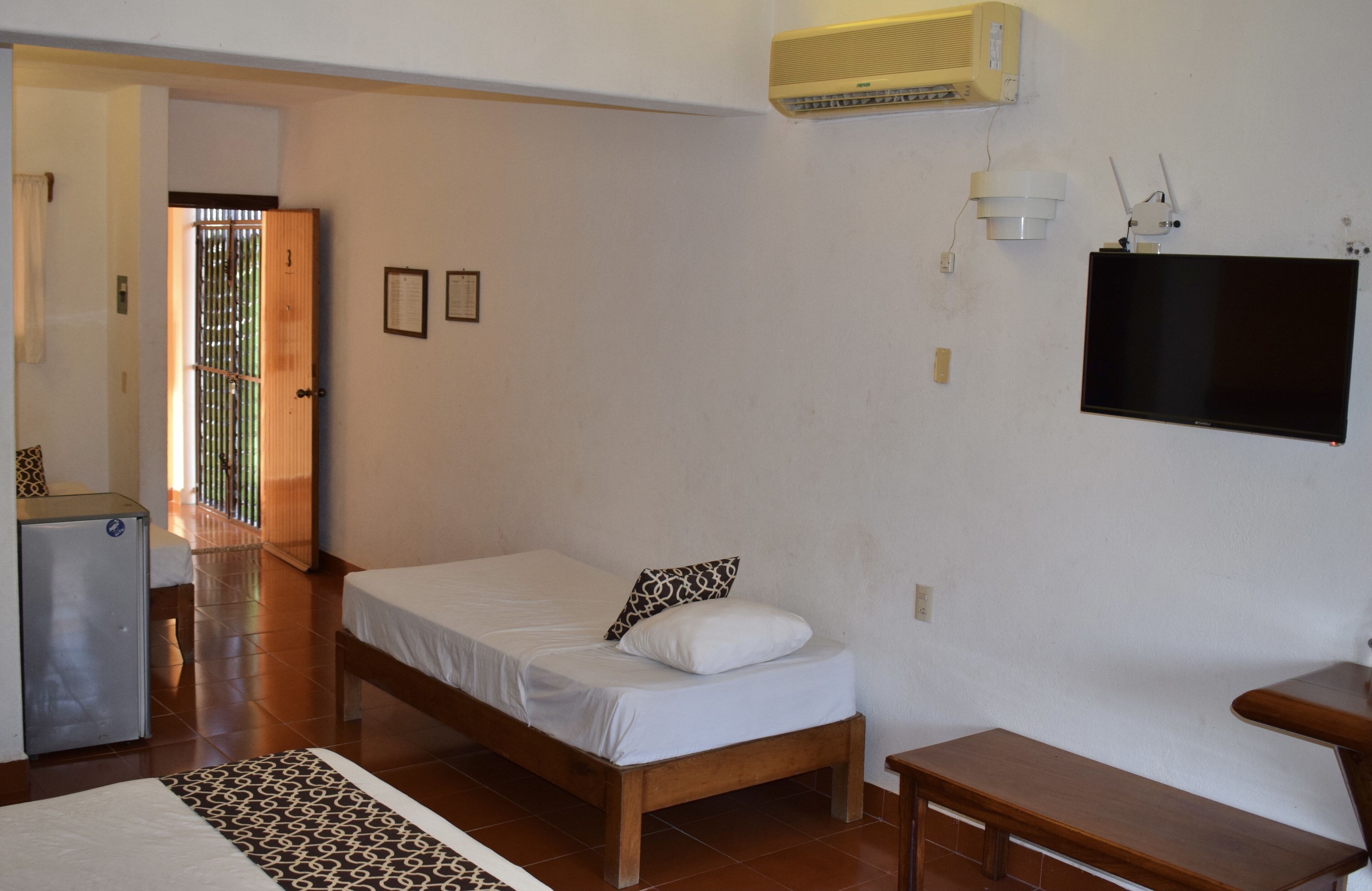 Ein Zimmer mit einem Bett, einem Schreibtisch, einem kleinen Kühlschrank und einem an der Wand befestigten Fernseher.