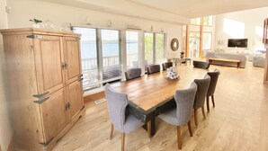 A spacious living area with a wooden dining table, grey upholstered chairs, a large wooden cabinet, and a television in the background.